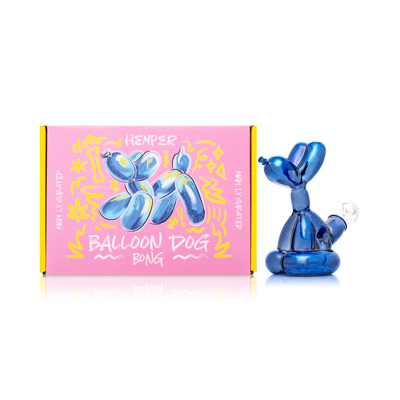Side view of Hemper Balloon Dog mini bong in iridescent blue glass posed next to matching pink Balloon Dog Bong gift box, studio lit.