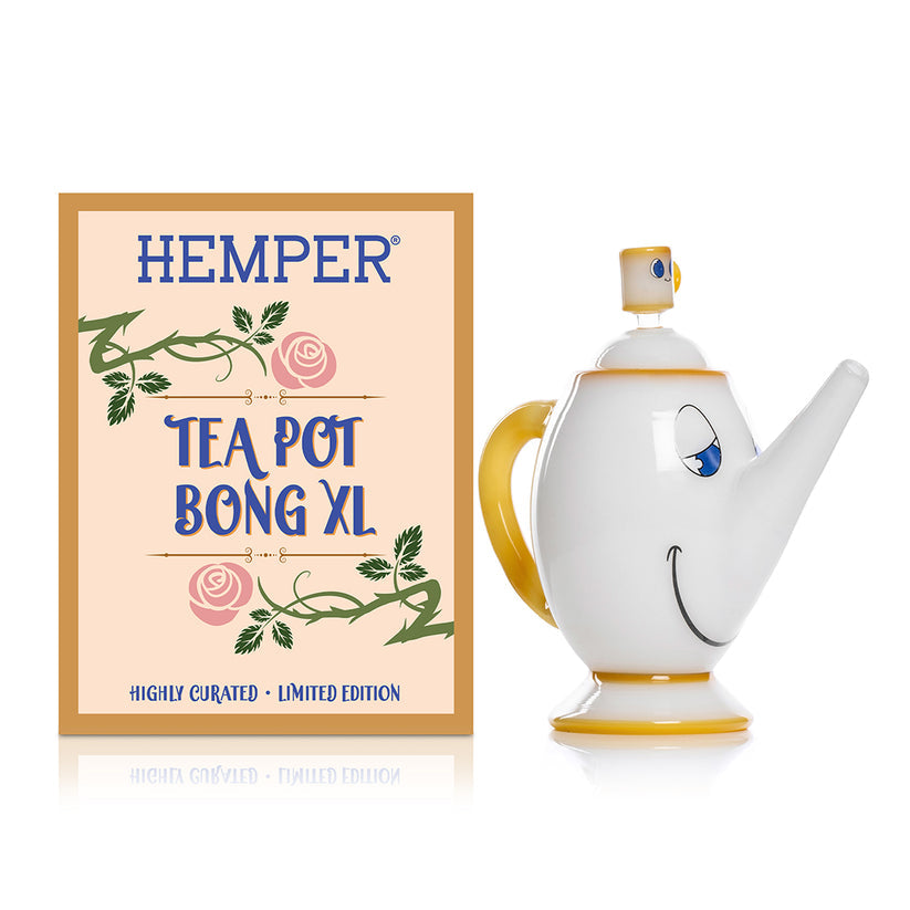 Front view of Hemper Tea Pot XL 8″ teapot glass bong with smiling face graphics next to matching floral retail box on white.