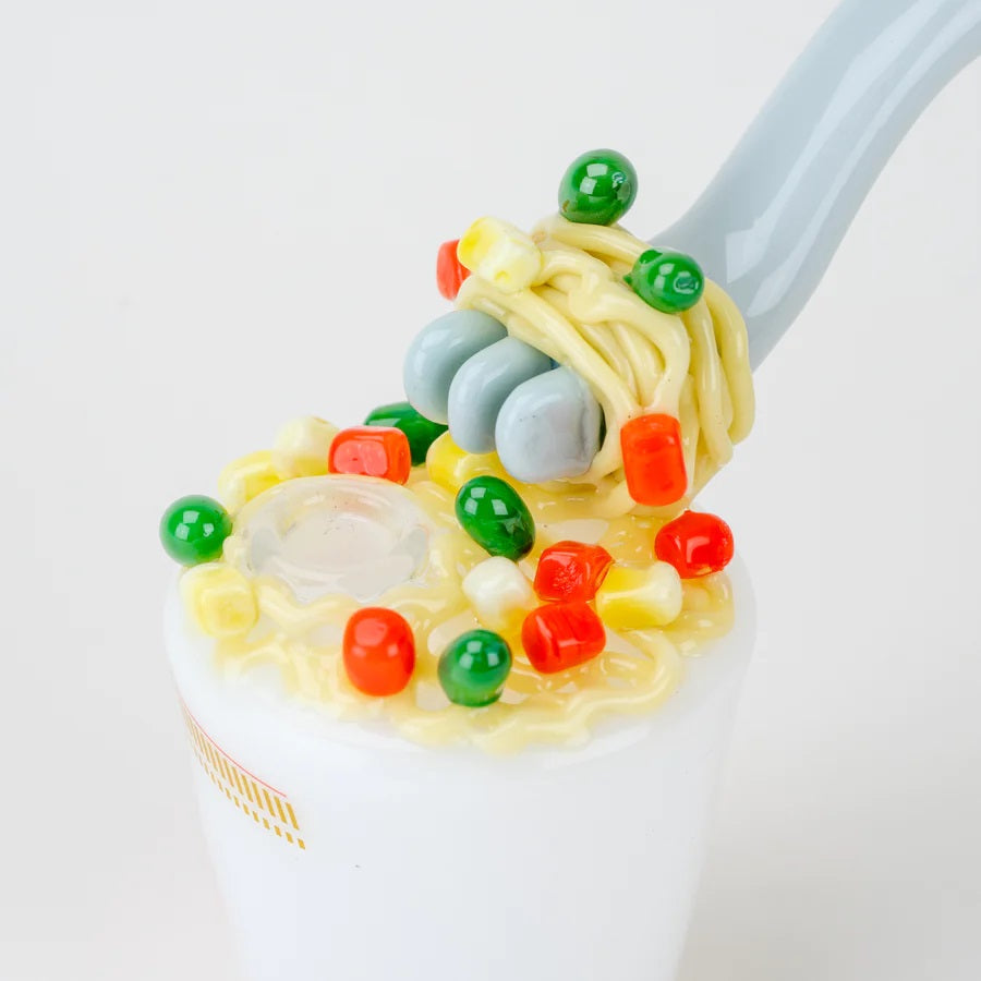 Overhead detail of sculpted noodles and veggies atop the cup, showing the curved fork mouthpiece entering the lid.