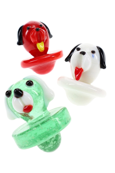 Trio of glass dog carb caps in red, white, and green with tongue-out faces and bubble bases for directional airflow on flat-top bangers.
