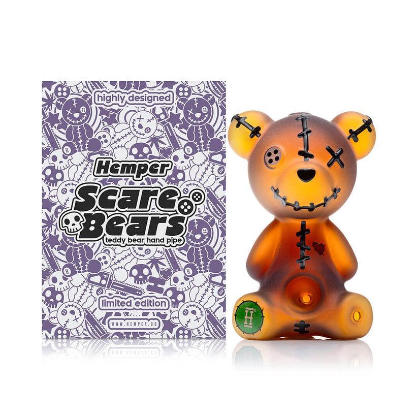 Front view of Hemper Scare Bears teddy bear hand pipe with amber frosted glass, black stitches and green logo foot on white.