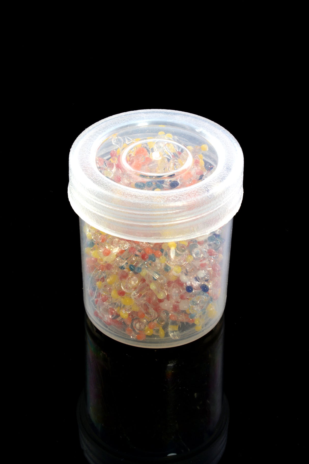Clear-lidded jar packed with multicolor glass daisy pipe screens, displayed on a glossy black surface.