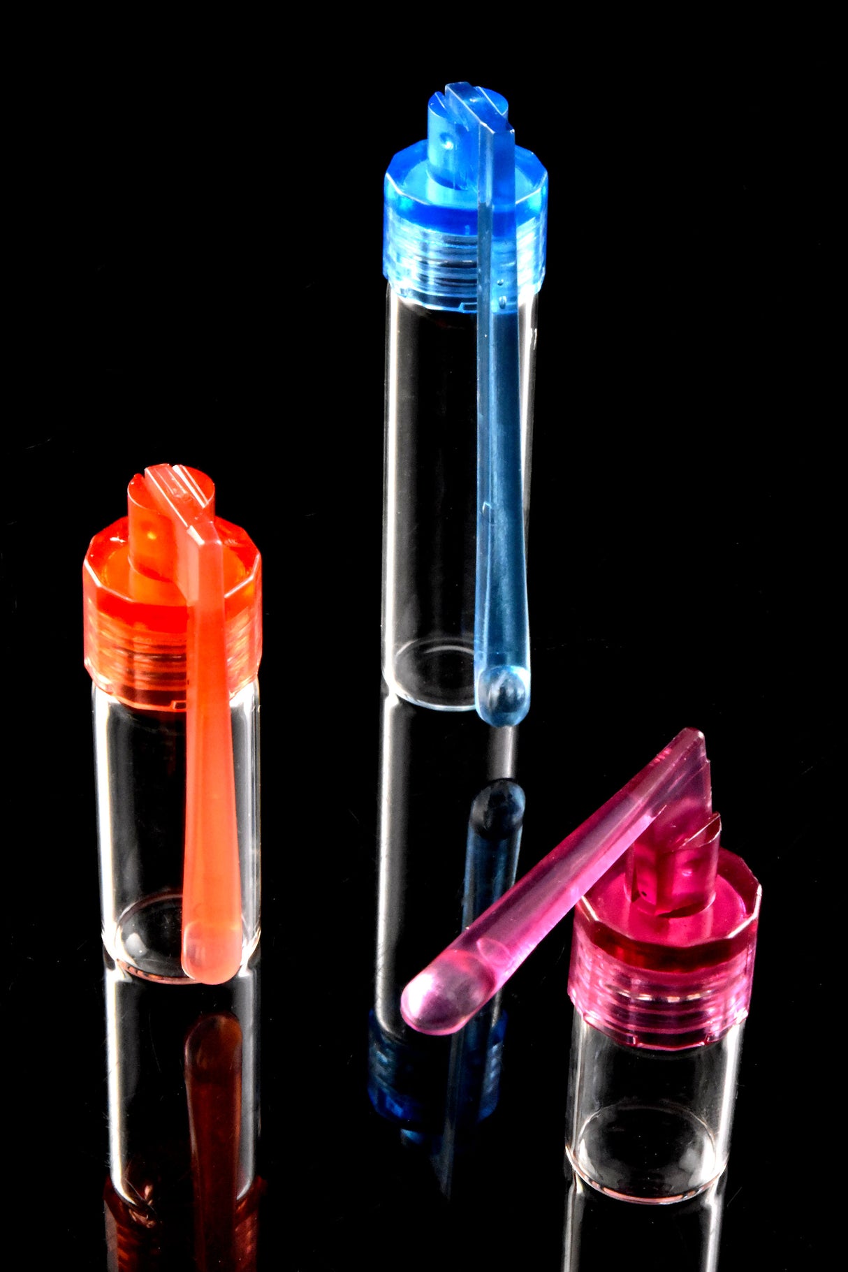 Blue, red and pink capped snuff vials with built-in dosing spoons, 38-67 mm tall, standing upright on glossy black surface.