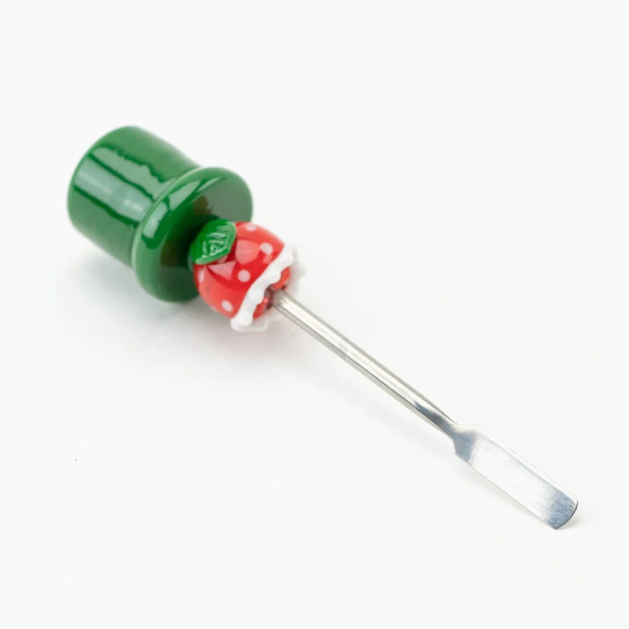Angled shot of piranha-plant glass dabber lying down, focusing on stainless blade and weighted green base on white surface.