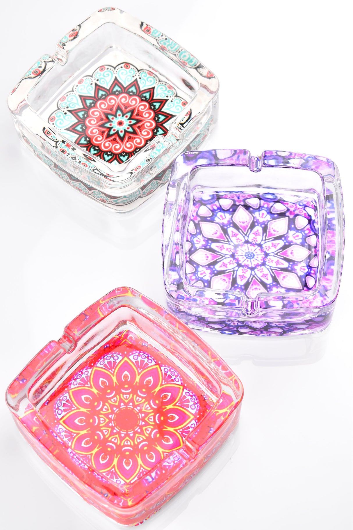 Square glass ashtray trio displaying pastel mandala patterns in aqua, lavender, and coral hues, overhead view.