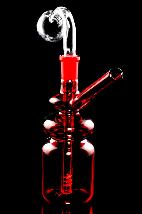 Red bottle oil burner rig featuring clear dome, glass-on-glass joint, and angled straw mouthpiece, black background.