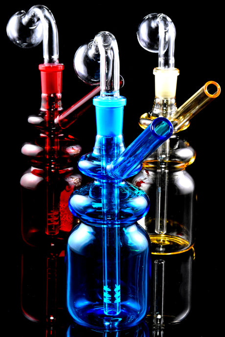 5½″ colored glass bottle oil burner rigs with angled straw mouthpiece and clear burner dome; assorted colors on black backdrop, sold individually.