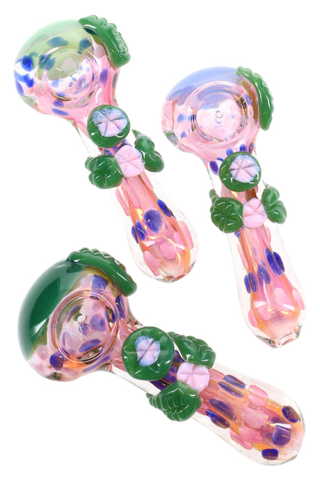Color-changing pink glass spoon pipe with raised green leaves, flower marbles, dotted inlays, and side carb; glossy finish; sold individually.