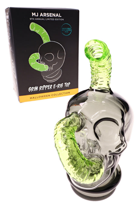 “Grim Ripper” Puffco Peak replacement glass by MJ Arsenal beside retail box, skull body with green intake tube and mouthpiece.