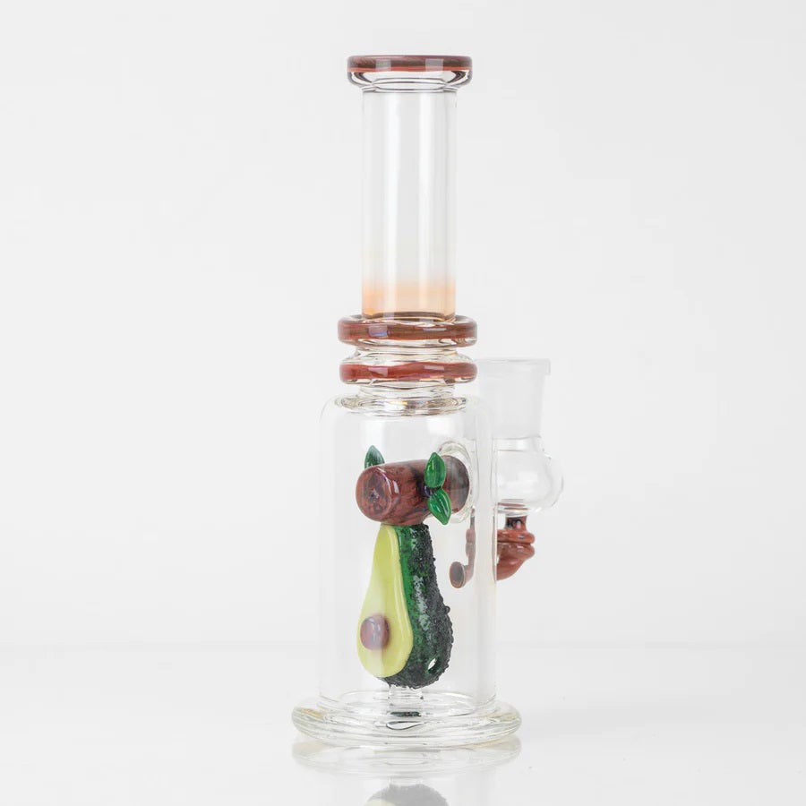 Avocado sculpture inside a compact clear mini tube on black background, showing wood-grain accents and flat stable base.
