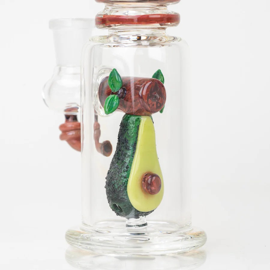 Close view of textured avocado sculpture and wood-grain log with green leaf details inside the glass chamber.