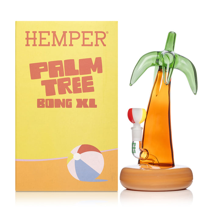 Palm tree bong staged beside Hemper retail box, amber-and-green glass with sand base and beach-ball bowl included