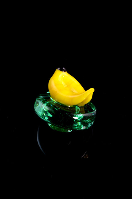 Banana carb cap resting on a translucent green base, whimsical glass accessory for directing airflow over hot concentrates.