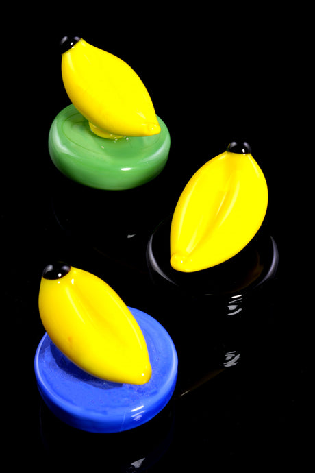Close-up of banana-themed glass carb cap on a green base, rounded shape with airflow hole for sealing a heated quartz bucket.