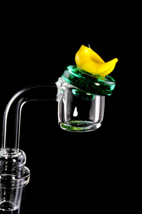 Banana glass carb cap shown atop a flat-top banger, sealing the bucket to retain heat and improve vapor on a dab rig.