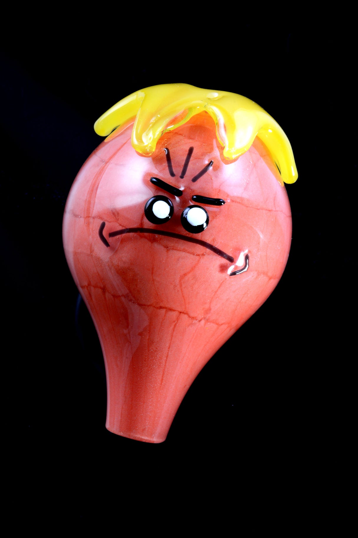 Front view of red bubble cap showing frowning cartoon face beneath yellow drip detail, clear tapered stem.
