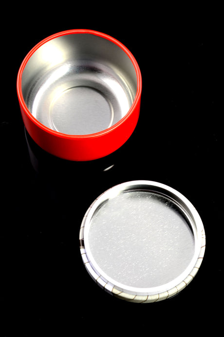 Open red metal stash container and printed lid resting on reflective black background, illustrating screw-top seal and spacious interior
