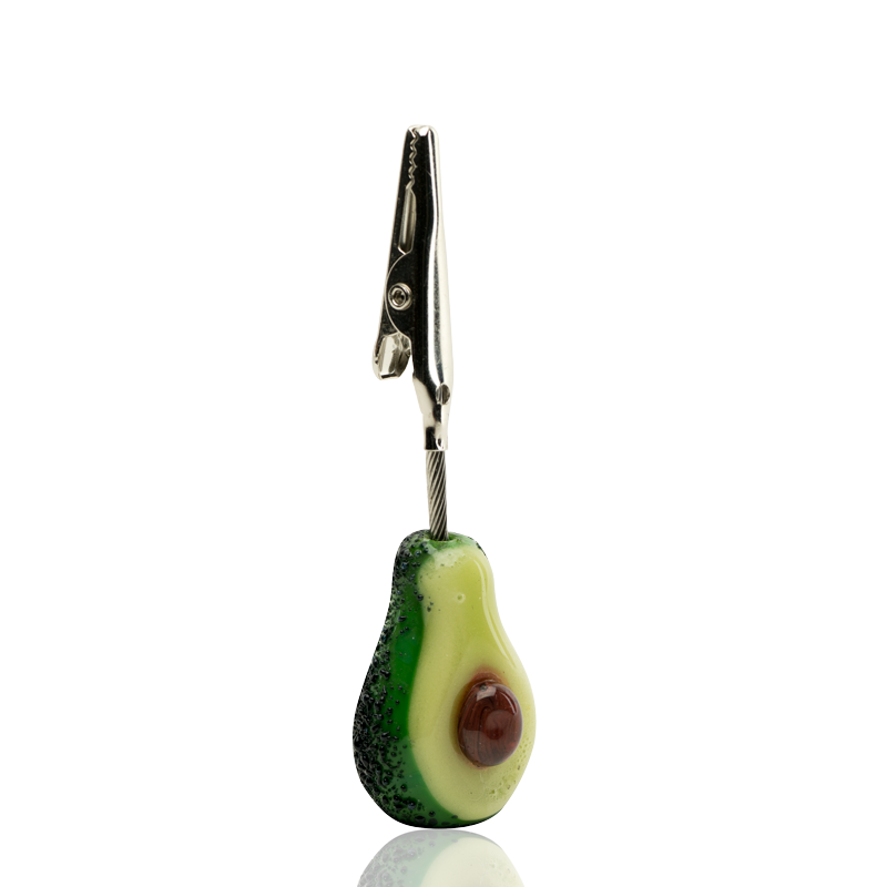 Side view of Empire Glassworks Avocadope glass roach clip showing detailed rind texture, glossy pit, and silver alligator clamp.