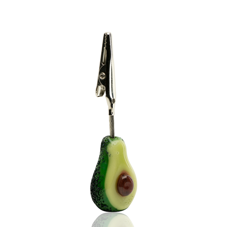Side view of Empire Glassworks Avocadope glass roach clip showing detailed rind texture, glossy pit, and silver alligator clamp.