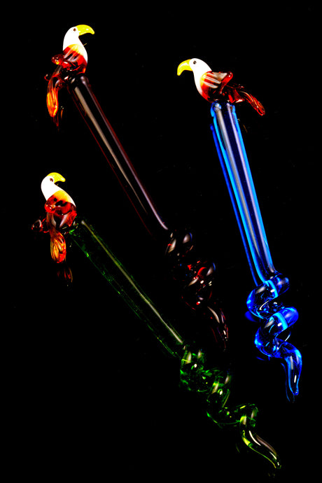 Three eagle-topped glass dabbers—crimson, cobalt, and forest hues—showing detailed bird heads and spiral tails, arranged on glossy black backdrop for dramatic contrast.