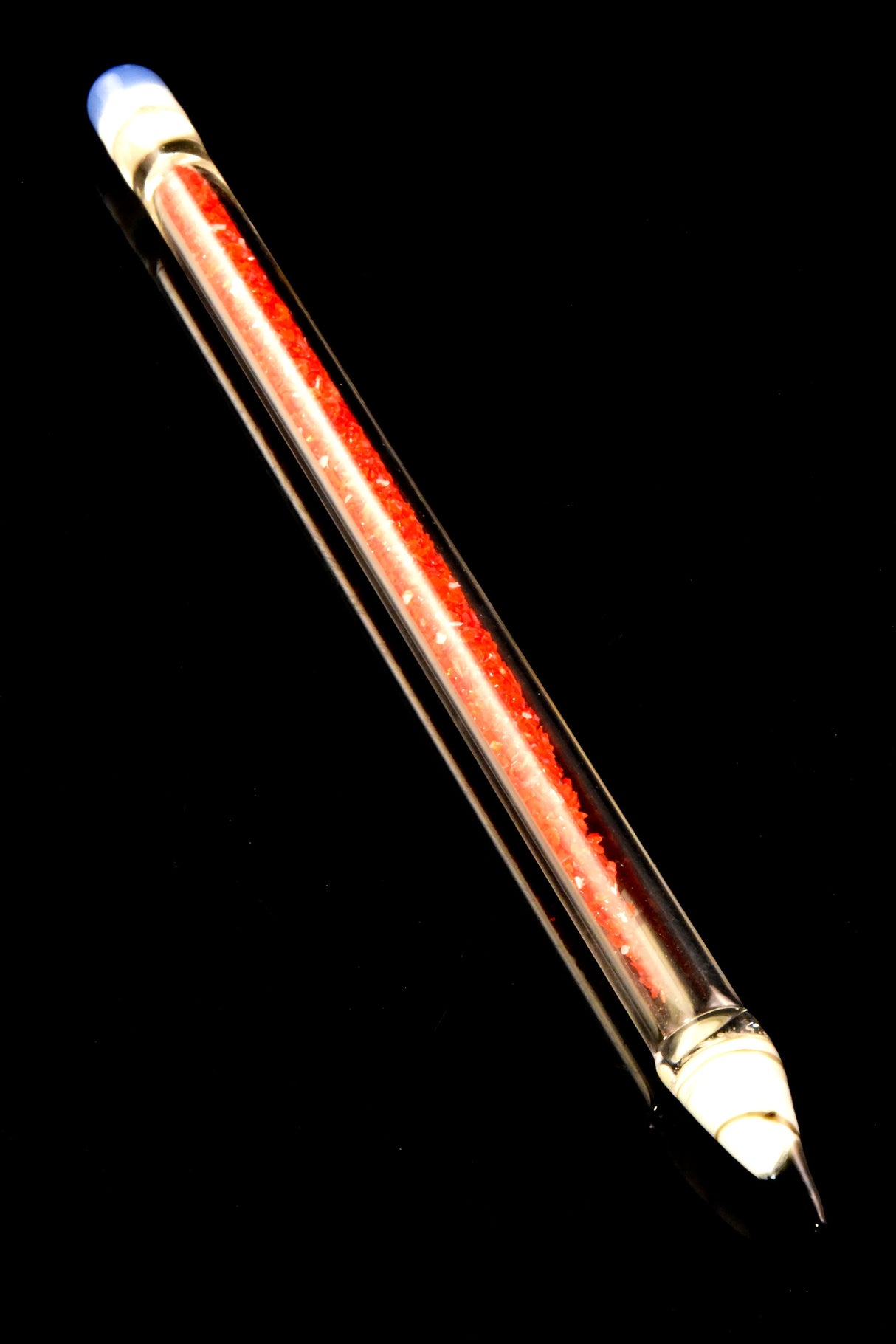 Single red-core glass pencil dab tool with vivid frit interior and precision glass tip, shown diagonally on reflective black background.