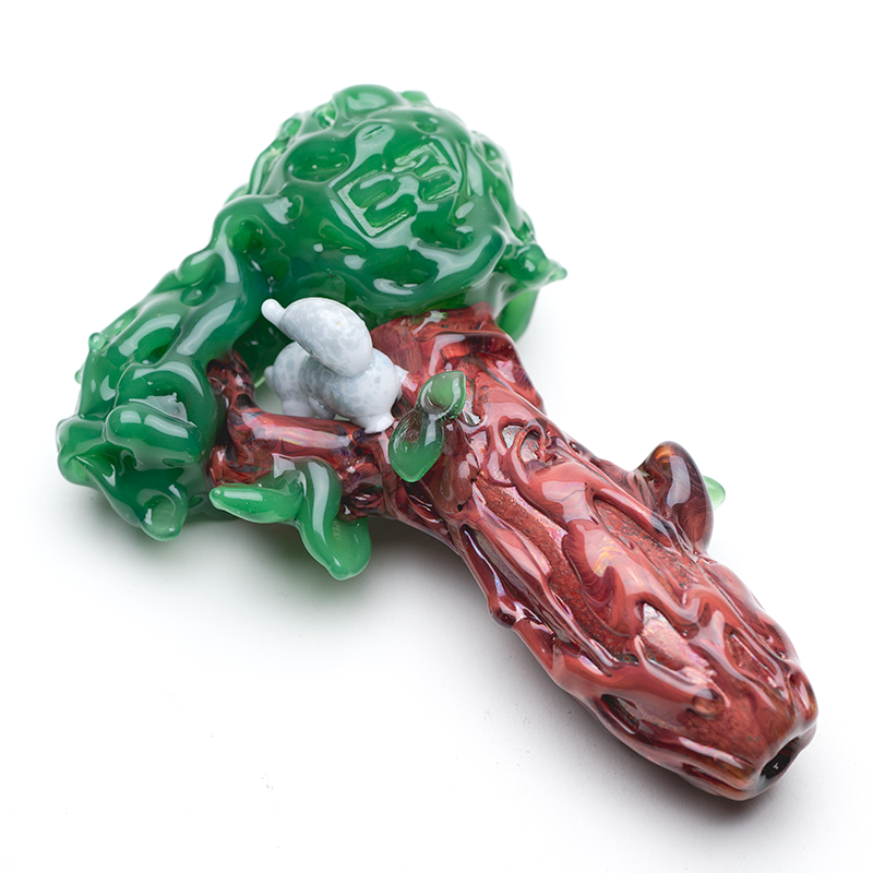 Rear angle of Squirrel’s Nest glass hand pipe showing brown trunk texture and green leafy canopy