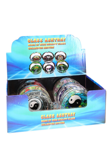 Front-facing view of blue retail display box holding yin-yang and cosmic design tempered glass ashtrays under studio lights.
