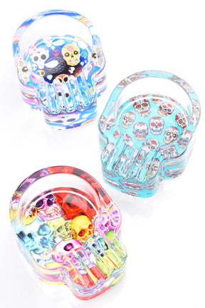 Trio of skull-shaped 3.5-inch glass ashtrays featuring vivid sugar-skull art in blue, aqua and rainbow tones, overhead studio photo.