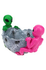 Pink and green alien duo gripping rugged silver crater-bowl resin ashtray, multiple cavity details and molded joint rests, studio white backdrop.