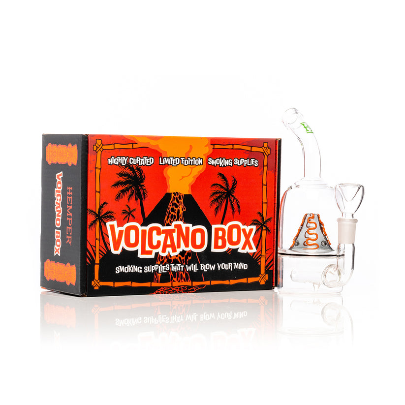 Hemper Volcano mini glass bong standing beside full-color Volcano Box, erupting mountain artwork and compact display-ready water piece.