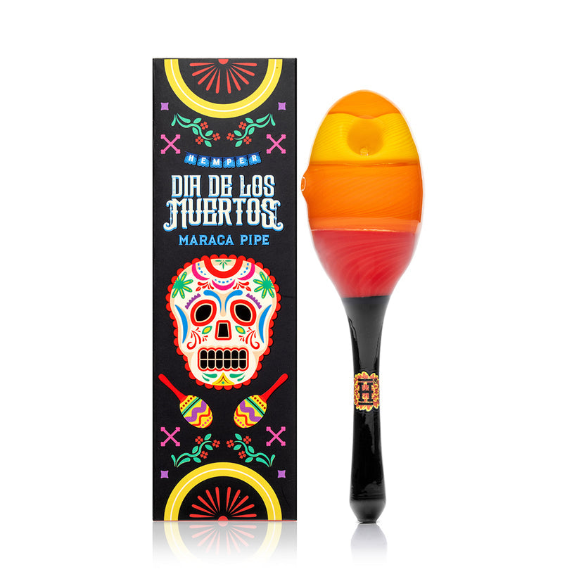 Front view of Hemper Dia De Los Muertos maraca hand pipe standing beside matching festival-themed box with bright skull artwork.