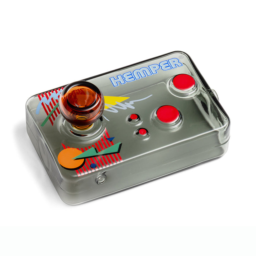 Angled overhead shot of Hemper arcade controller glass hand pipe showing amber joystick bowl, red buttons, and 80s-style graphics.