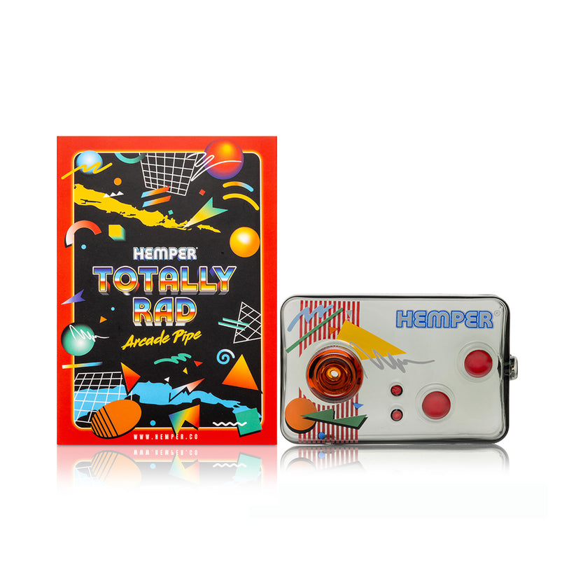 Front view of Hemper Totally Rad arcade controller glass hand pipe beside matching neon arcade-themed retail box on white surface.