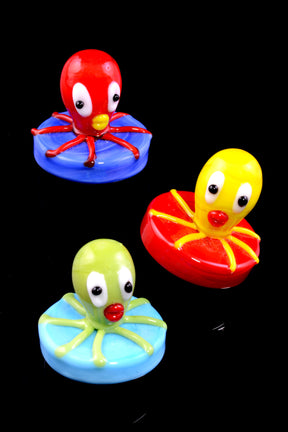 A set of three colorful glass carb caps shaped like octopi, with one in red, one in blue, and one in green.