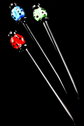 rio of 5-inch glass dab tools with black stems and red, blue, and green ladybug toppers, arranged diagonally on black background for vivid contrast.