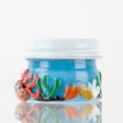 Side profile of blue under-the-sea glass terp jar featuring coral, sea grass and cute squid sculpted in hot glass with white screw lid, on white background