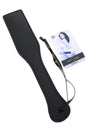 Black 12.5-inch faux leather BDSM paddle shown angled with textured surface, wrist strap and hang tag