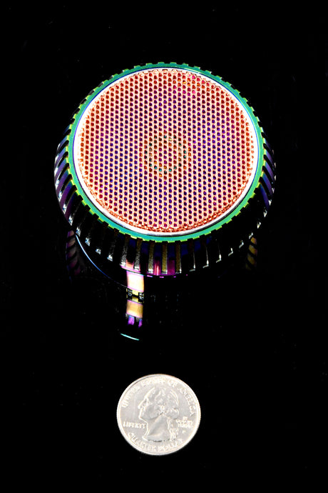 Top view of rainbow grinder cap with perforated texture beside a quarter for scale, compact 2½-inch diameter.