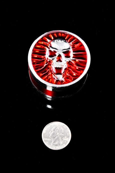 Compact red skull-design 3-part metal grinder shown with a quarter for size reference, approximately 2 inches in diameter.