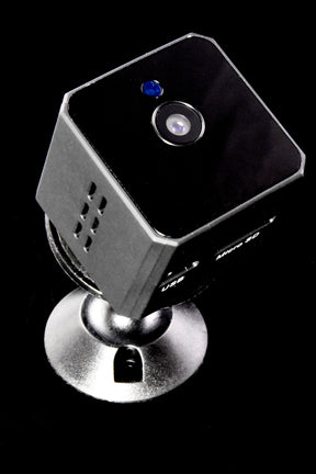 Compact HD surveillance cube on black reflective surface, infrared sensor lens and blue status light facing camera on metal base