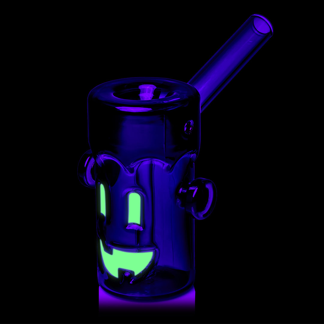 MJ Arsenal Frankenbubbler glass bubbler under UV light with glowing face, black hair and angled mouthpiece