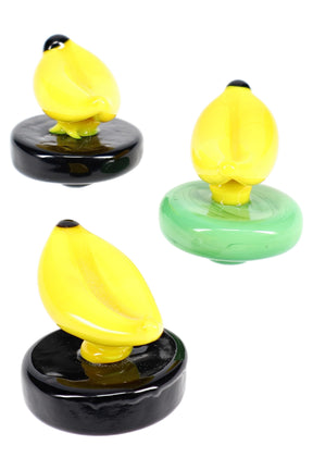 Glass banana carb cap with bright yellow fruit topper on a round colored base; novelty cap that helps control airflow over the bucket.