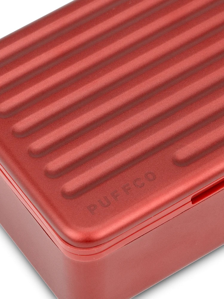 Macro shot of Puffco Daybreak Travel Case ridged aluminum lid finished in matte red, subtle Puffco logo engraved near corner.