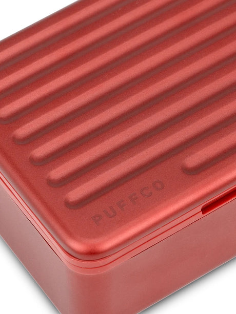 Macro shot of Puffco Daybreak Travel Case ridged aluminum lid finished in matte red, subtle Puffco logo engraved near corner.