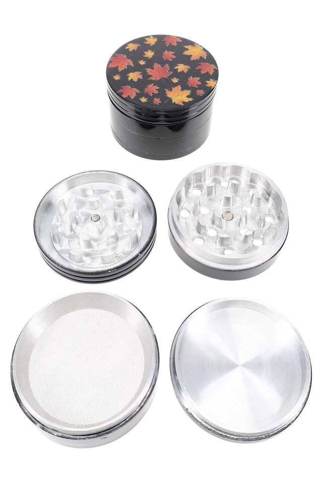 Black 56 mm 4-part aluminum herb grinder with fall-leaf decal lid, shown disassembled with teeth, mesh sifter and catch.