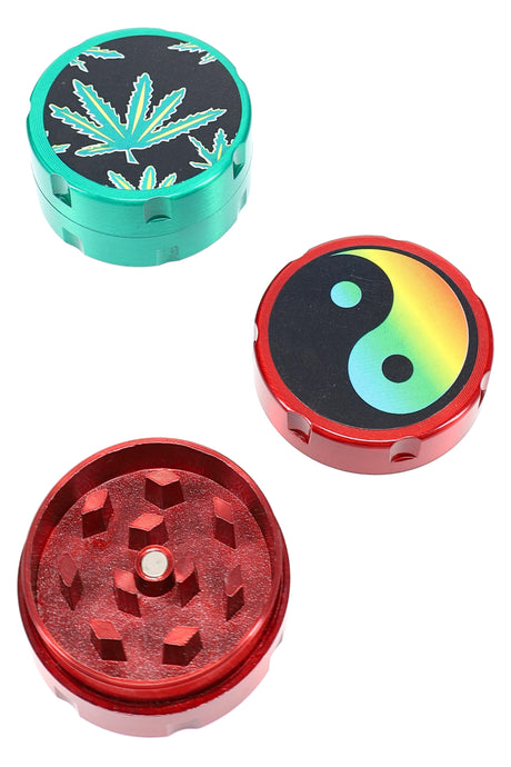 Small 2-part metal herb grinder with teal leaf-decal lid and red base shown apart; compact 30 mm (1¼″) size.