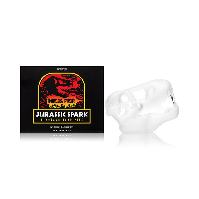 Side-by-side shot of Hemper Jurassic Spark skull hand pipe and branded box, highlighting compact dinosaur design for home smokers.