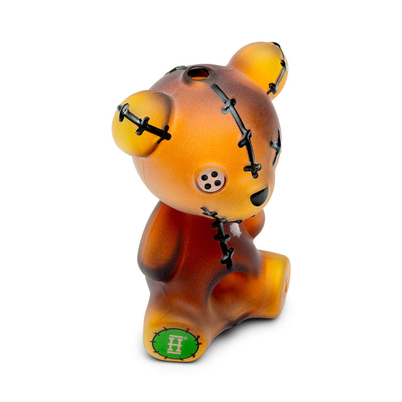 Angled view of Hemper Scare Bears amber teddy bear glass hand pipe with button eye, stitched seams and compact sitting shape.