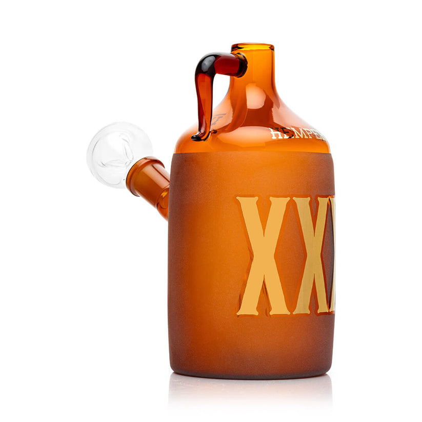 Side profile of amber Wild West moonshine bottle glass bong showing frosted XXX wrap, clear 14.5 mm bowl, and curved jug-style handle.