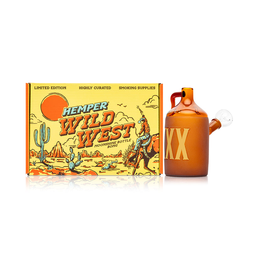 Wide shot of Hemper Wild West Moonshine Bottle bong standing beside matching cowboy scene box, centered on a clean white background.